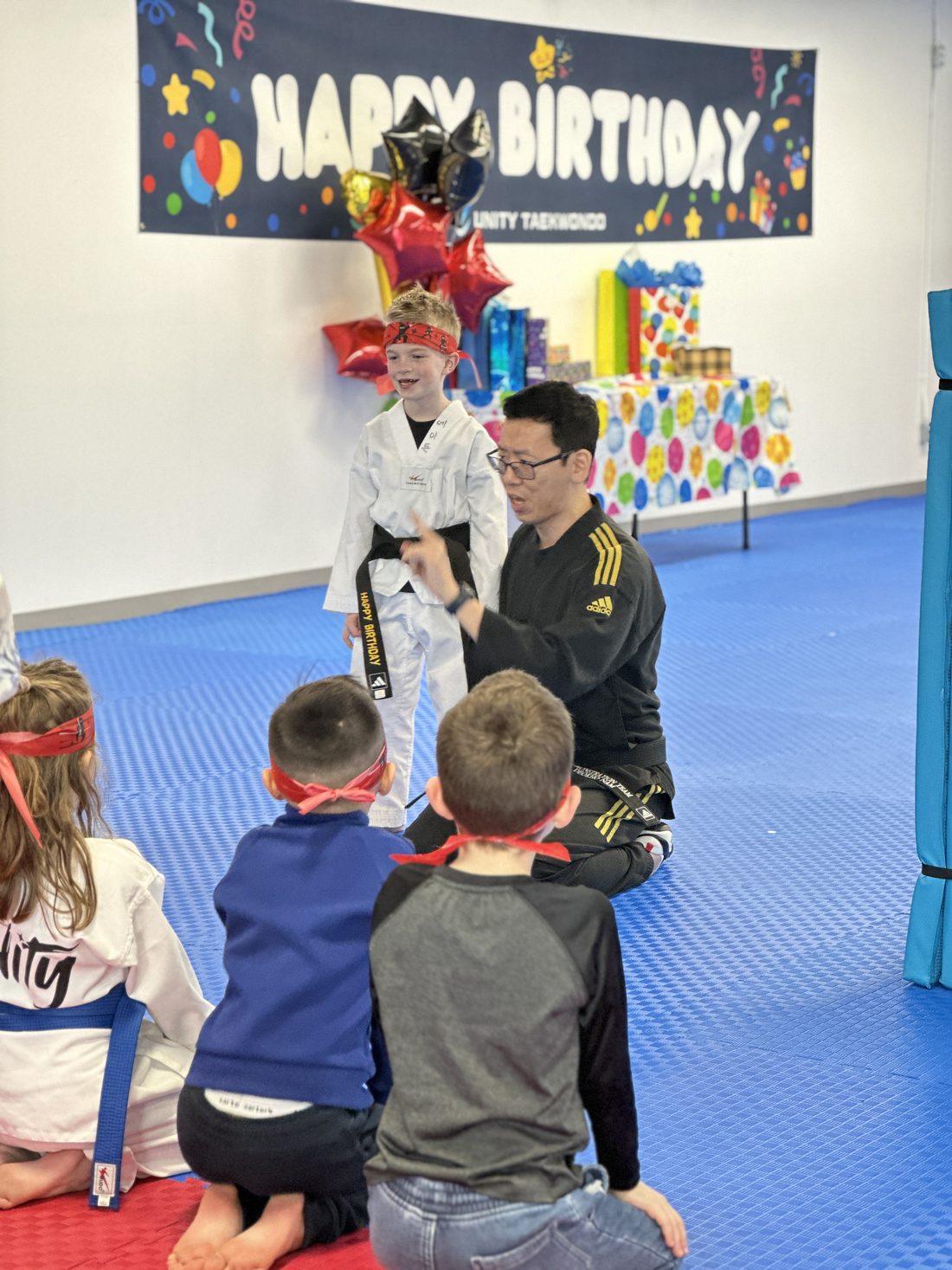 Instructor with the birthday child wearing a crown in front of the Happy Birthday banner at Unity Taekwondo